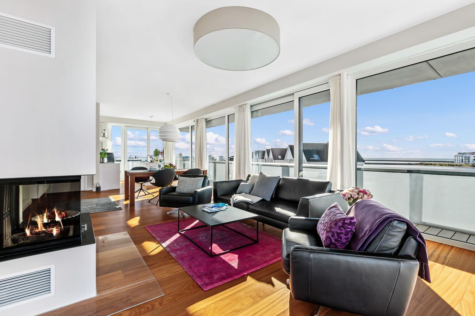 Wohnbereich mit Kamin, Ledersofa und großem Fensterblick auf Wasser.