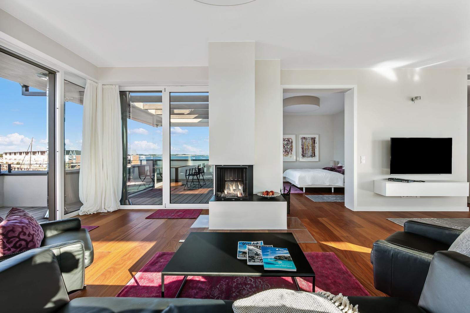Wohnbereich mit Kamin, TV und Blick auf Balkon mit Meerblick.