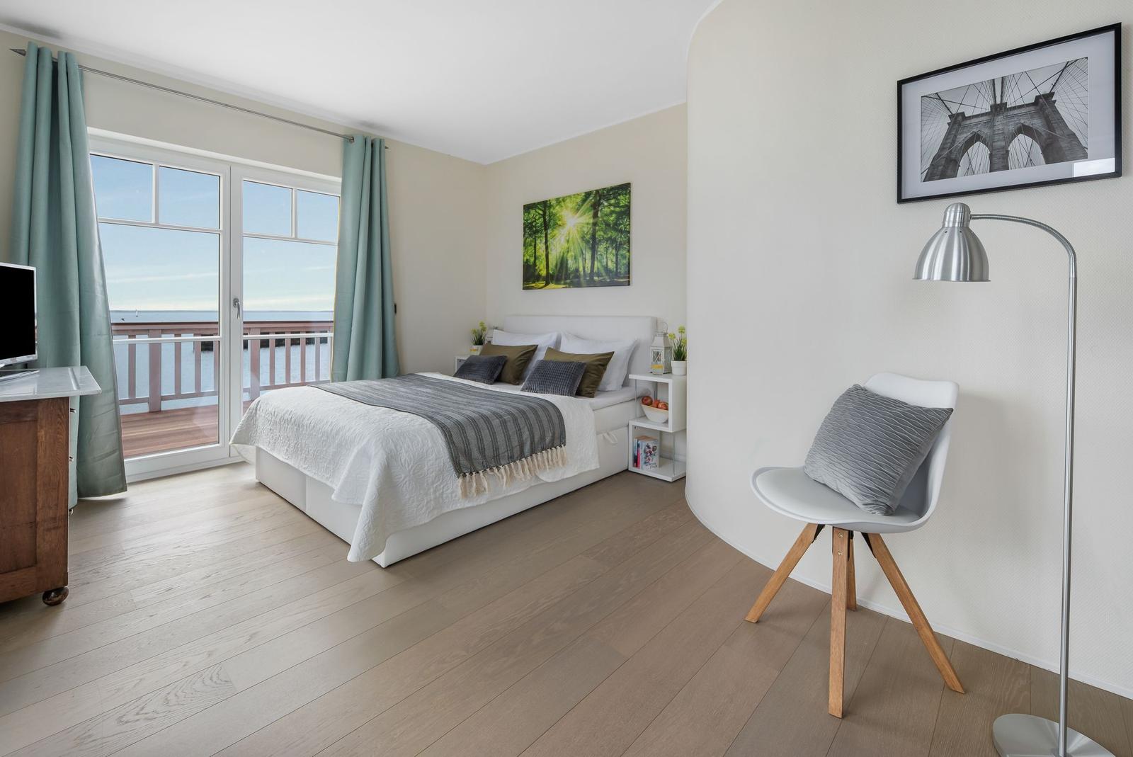 Schlafzimmer mit Balkonblick, Bett, Stuhl und Stehlampe.