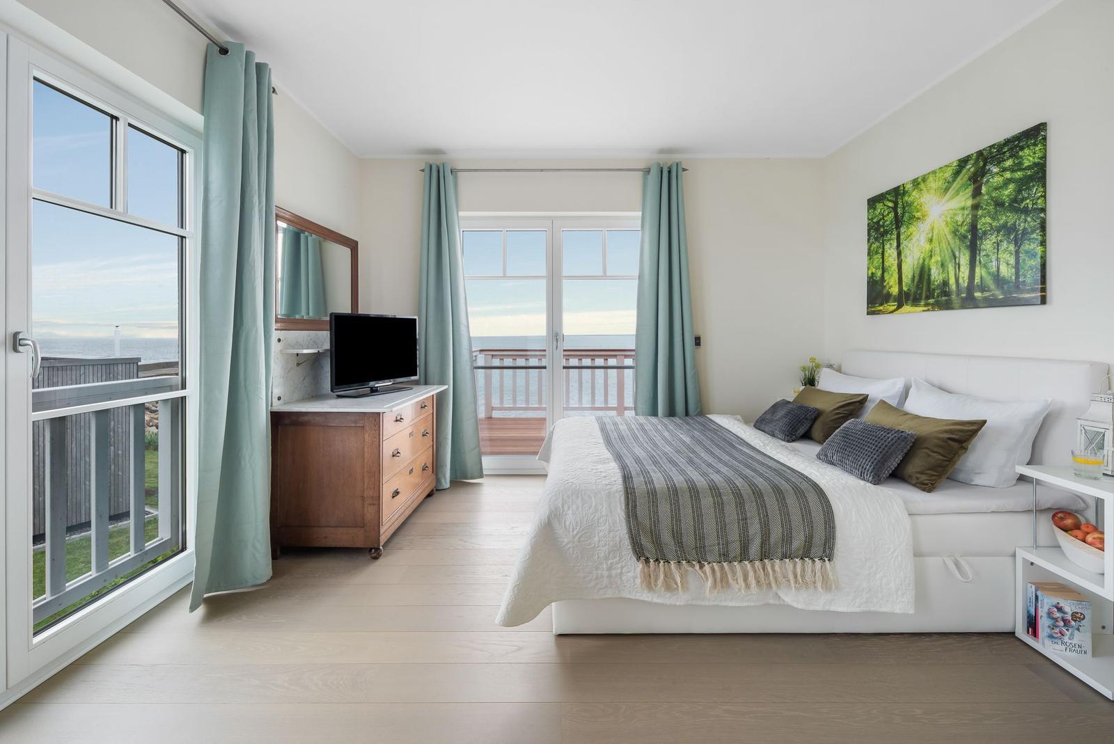 Schlafzimmer mit Bett, Fernseher und Blick aufs Meer.