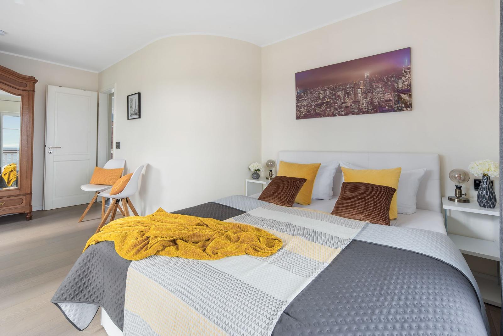 Schlafzimmer mit Bett, Wandbild und Nachttischen. Holzfußboden und Spiegel.