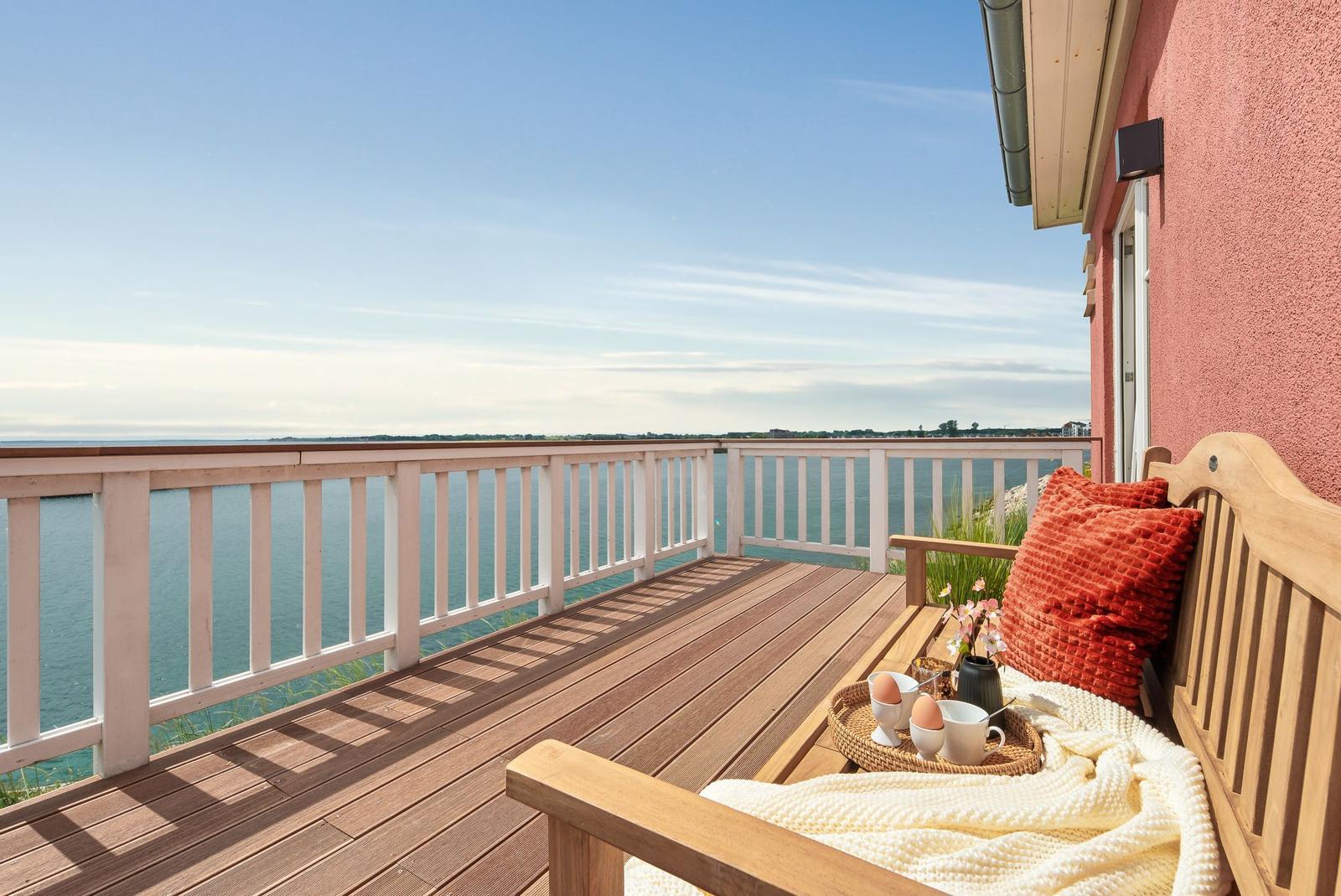 Terrasse mit Blick auf das Meer und Holzbank mit Kissen und Decke.
