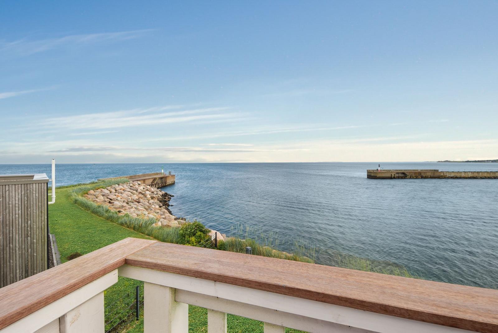 Blick von Balkon auf Meer mit Steinhafeneinfassung und grüner Fläche