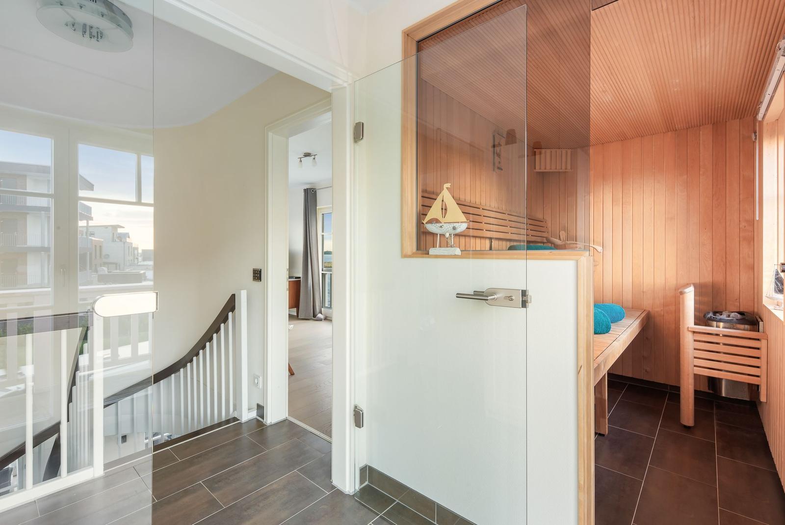 Sauna mit Holzwand und Bank, Glaswand, Treppenhaus und Fenster sichtbar.