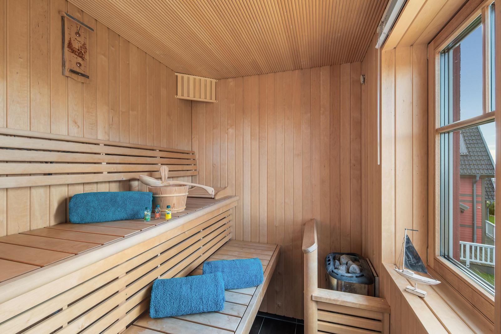 Sauna mit Holzbank, blauen Handtüchern und Blick auf Außenbereich.