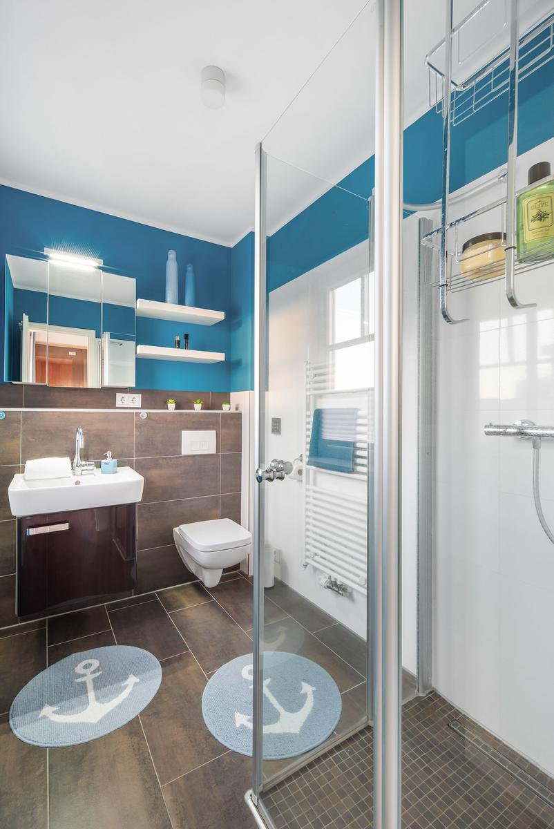 Badezimmer mit Dusche, Waschbecken und Toilette. Blaue Wände und runde Teppiche mit Ankern.