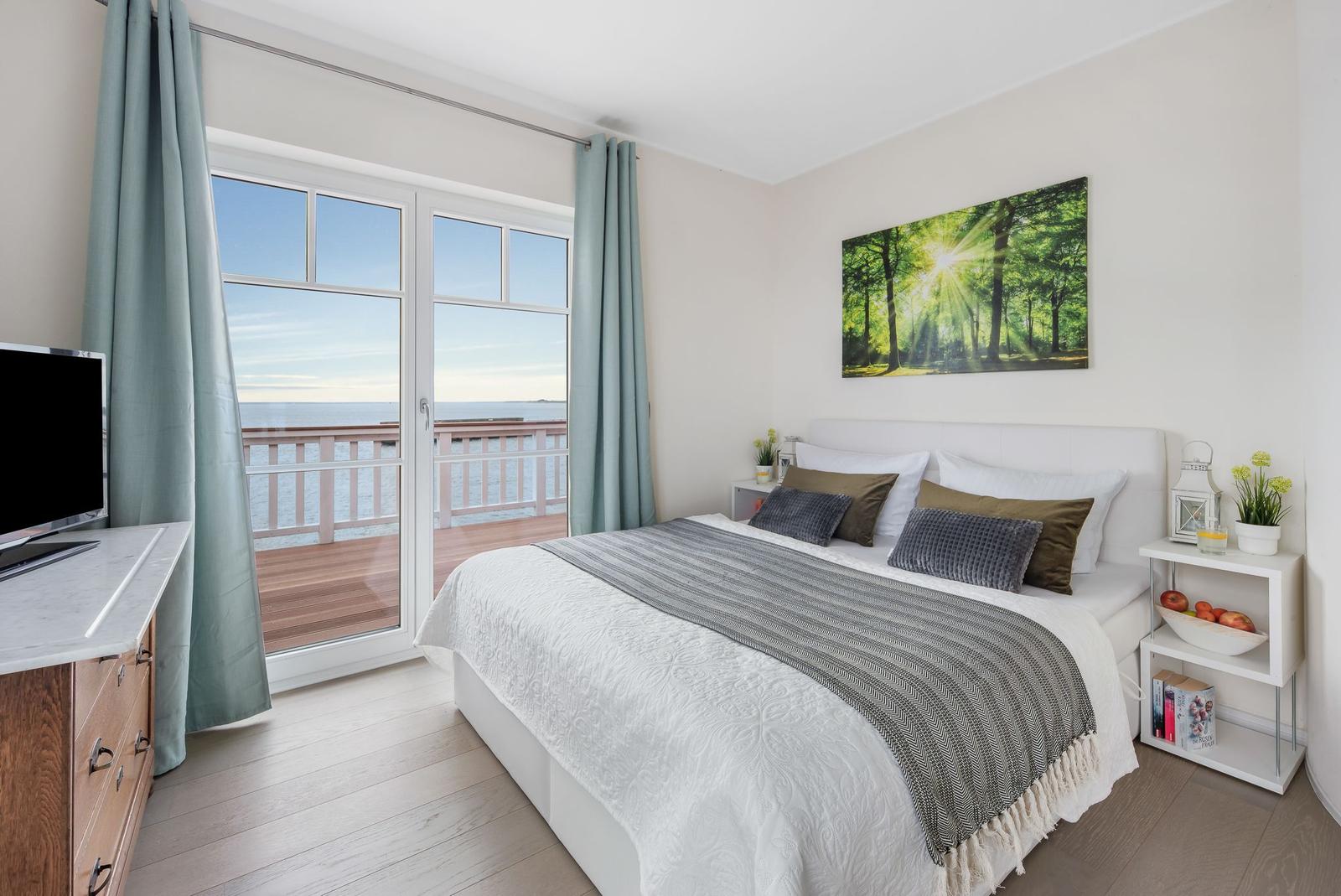 Schlafzimmer mit Blick aufs Meer und Balkon. Bett, Nachttische und Fernseher.