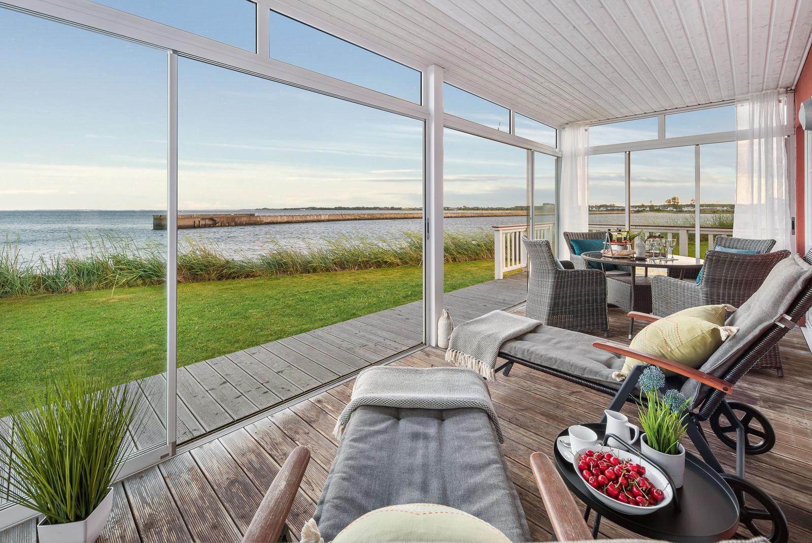 Terrasse mit Loungemöbeln und Blick auf Wasser und Grasfläche.