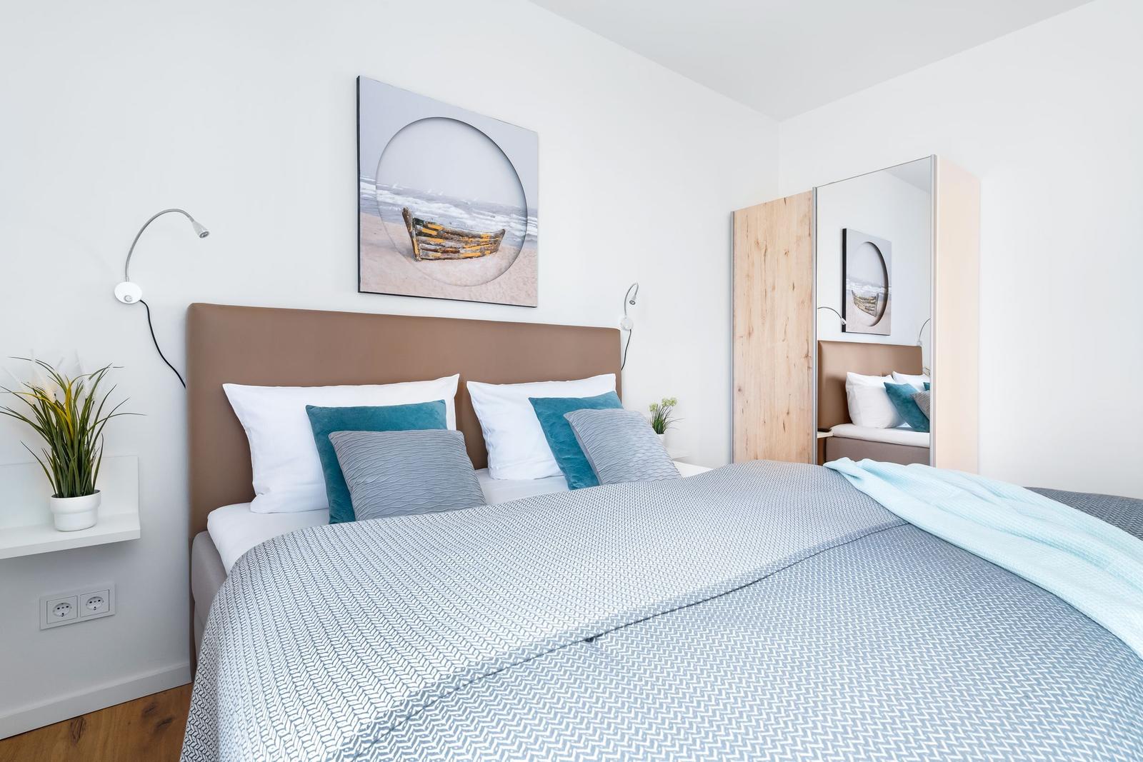 Schlafzimmer mit Bett, Wandbild und Spiegelschrank.