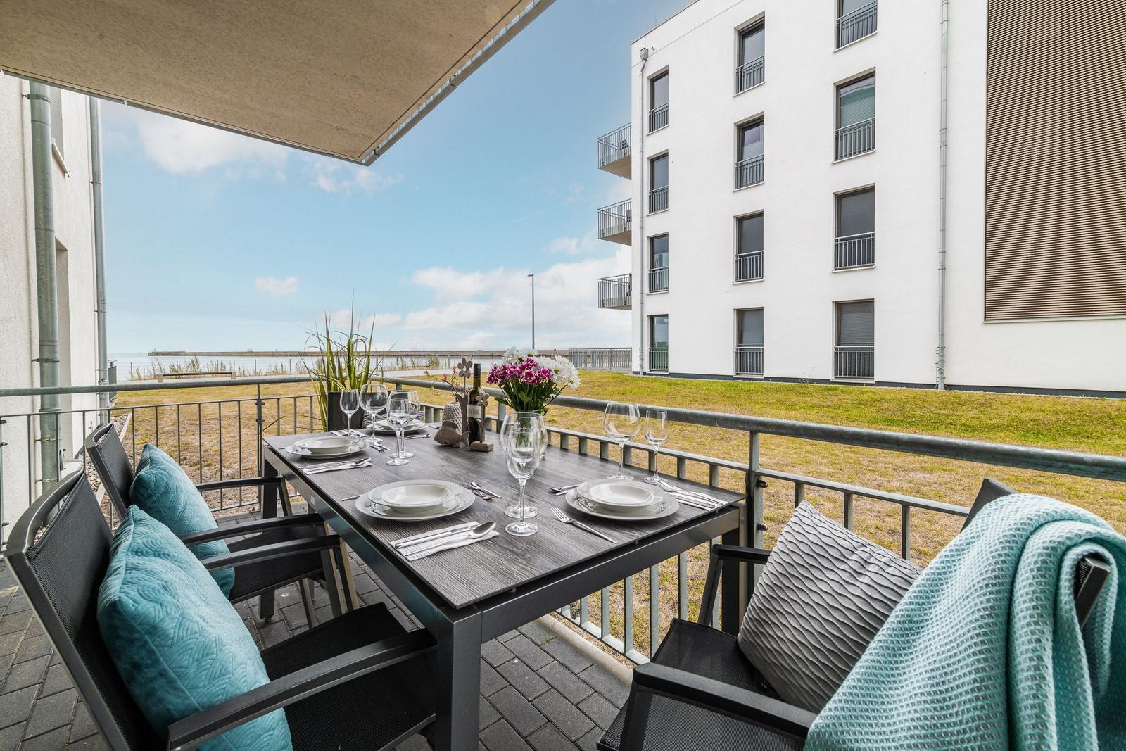 Terrasse mit Tisch, Stühlen und Blick auf Wasser und Gebäude.
