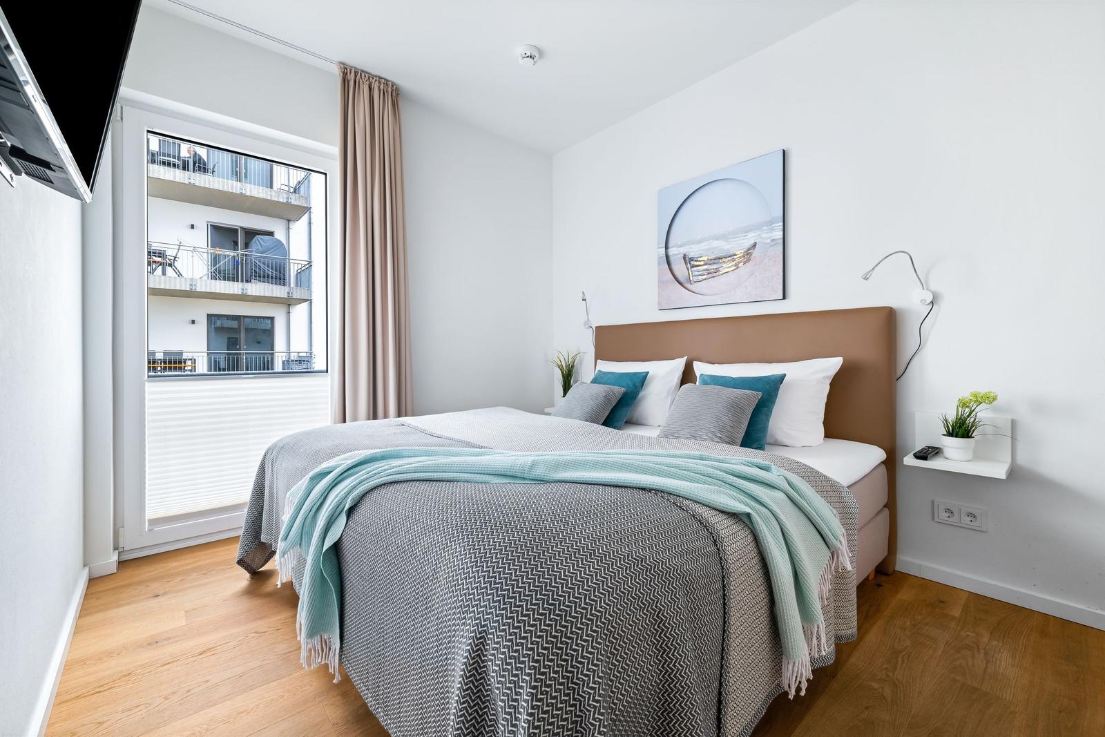 Schlafzimmer mit Bett, Wandbild und Fenster zur Aussicht.