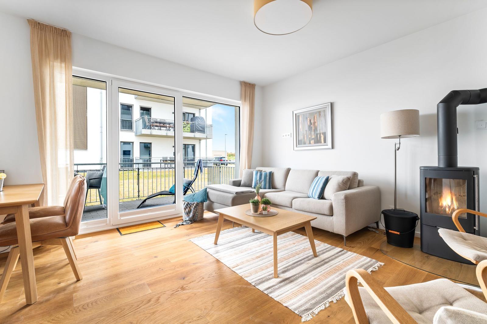 Wohnzimmer mit Sofa, Kamin und Terrasse. Holzboden und große Fenster.