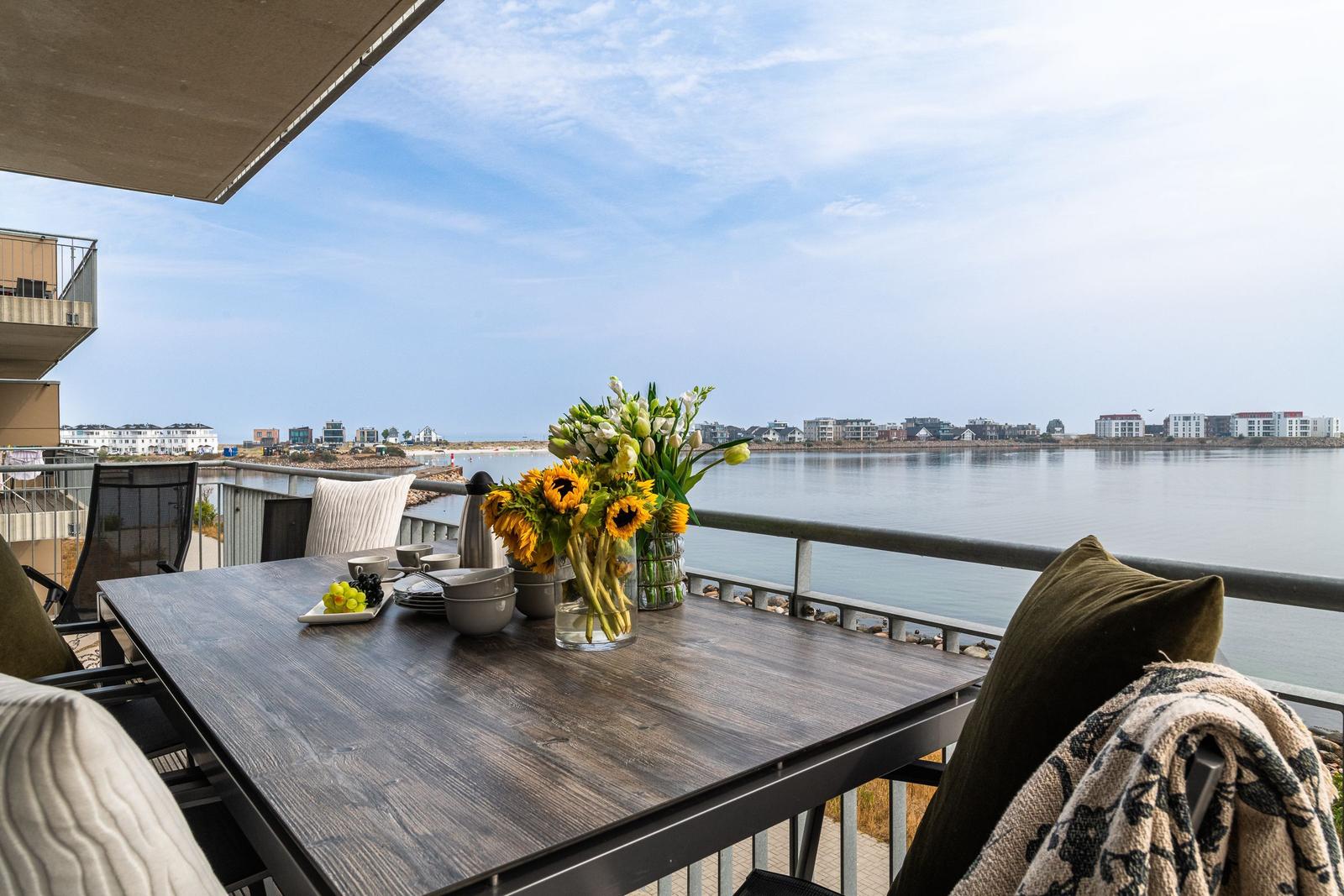 Terrasse mit Tisch, Stühlen und Blick auf Wasser und Gebäude