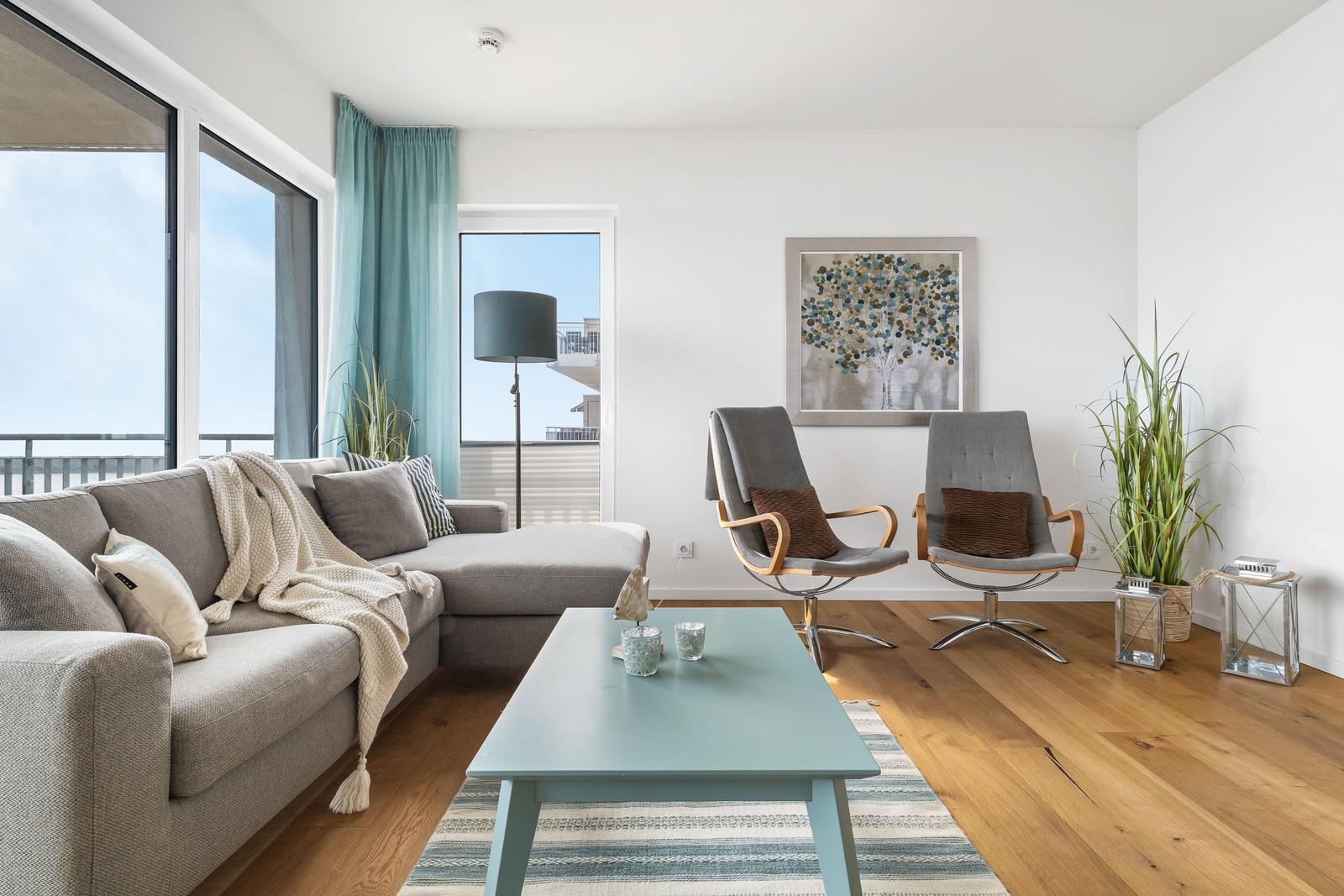 Wohnzimmer mit Sofa, zwei Sesseln, Tisch und Blick auf Balkon.