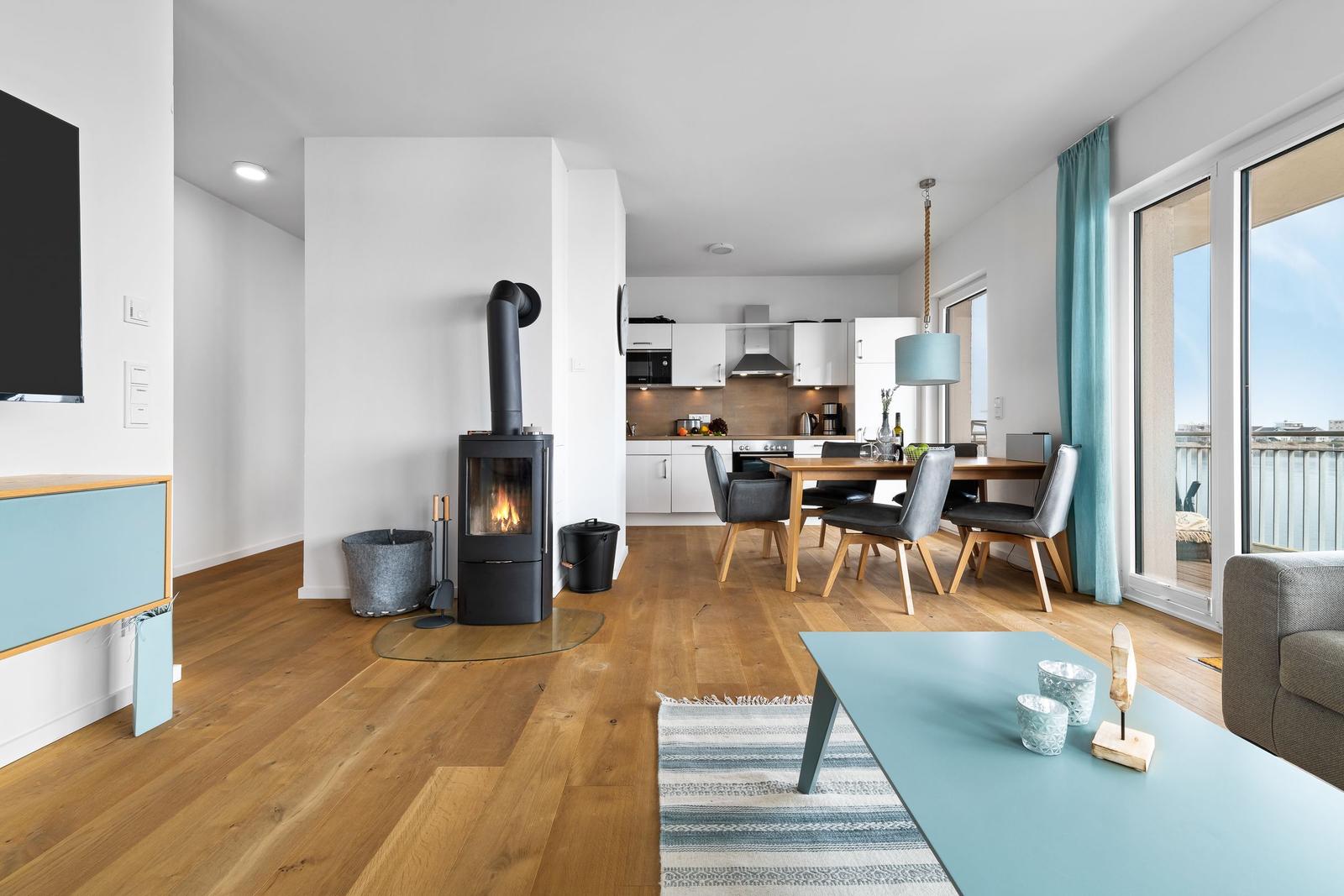 Wohnzimmer mit Kamin, Essbereich und Küche. Holzboden und große Fenster.