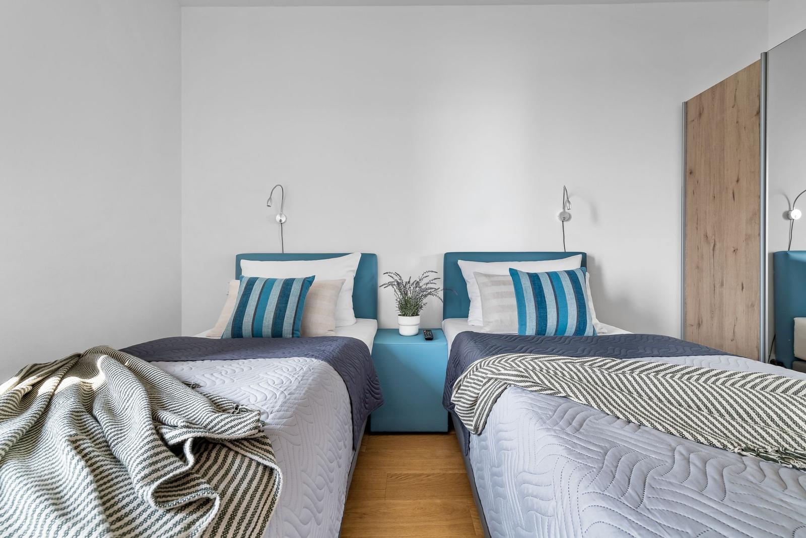 Zwei Einzelbetten mit blauen Kopfteil und Nachttisch in einem Schlafzimmer.