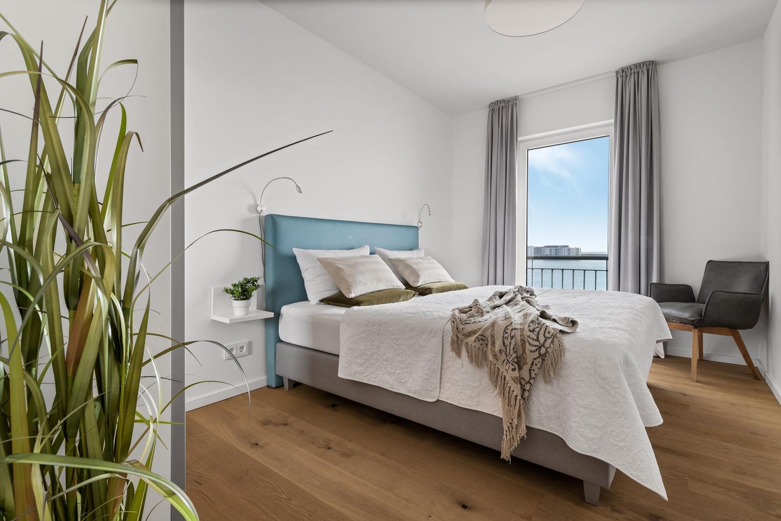 Schlafzimmer mit Bett, Fensterblick auf Wasser und Stuhl.