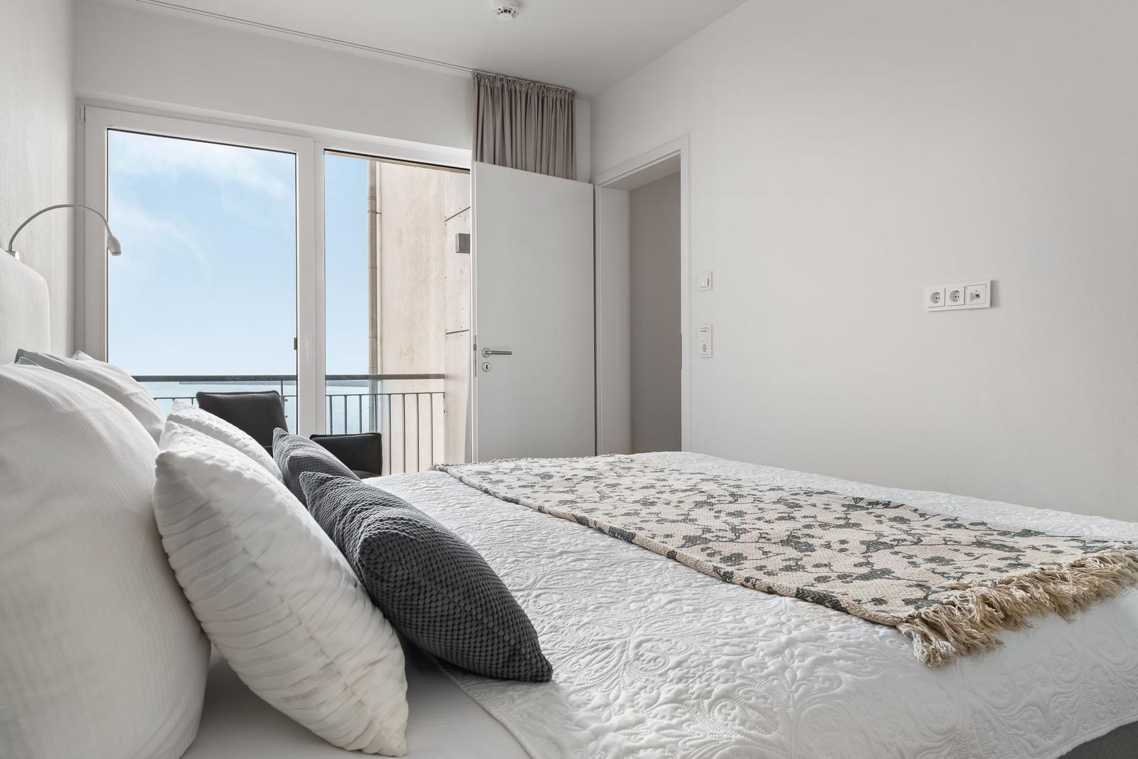 Schlafzimmer mit Balkon und Blick auf Meer. Bett mit Kissen und Decke.