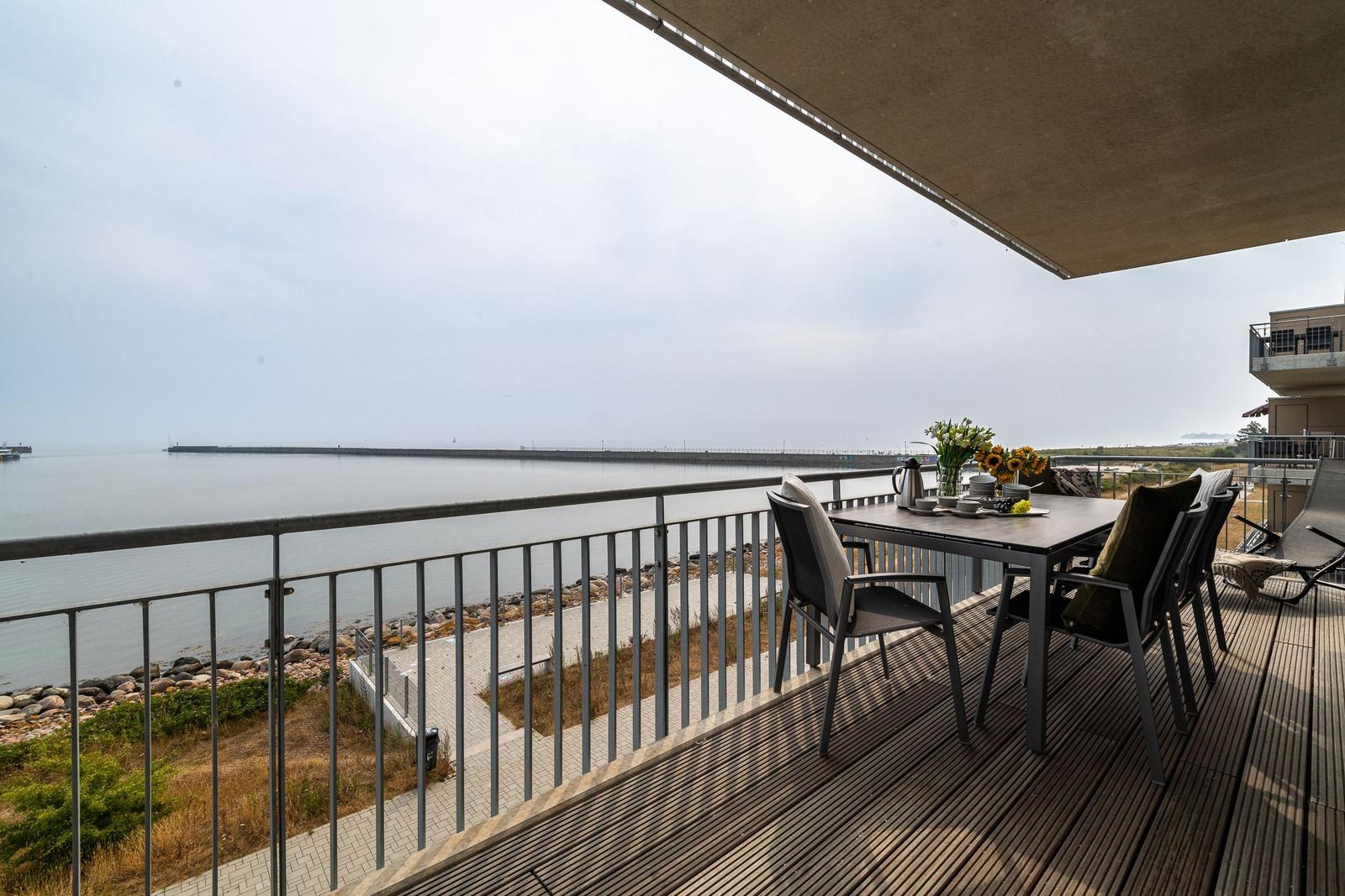 Terrasse mit Tisch und Stühlen überblickt die Küste und den Hafen.