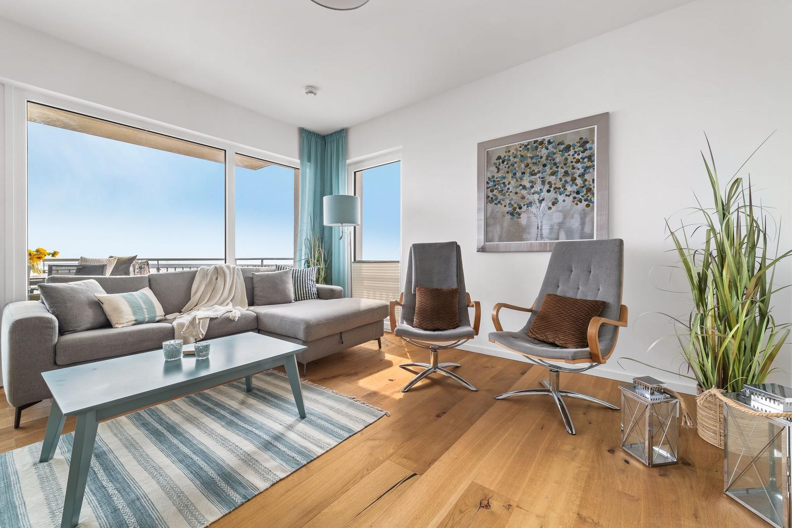Wohnzimmer mit Sofa, zwei Sesseln, Couchtisch und Blick auf Balkon.