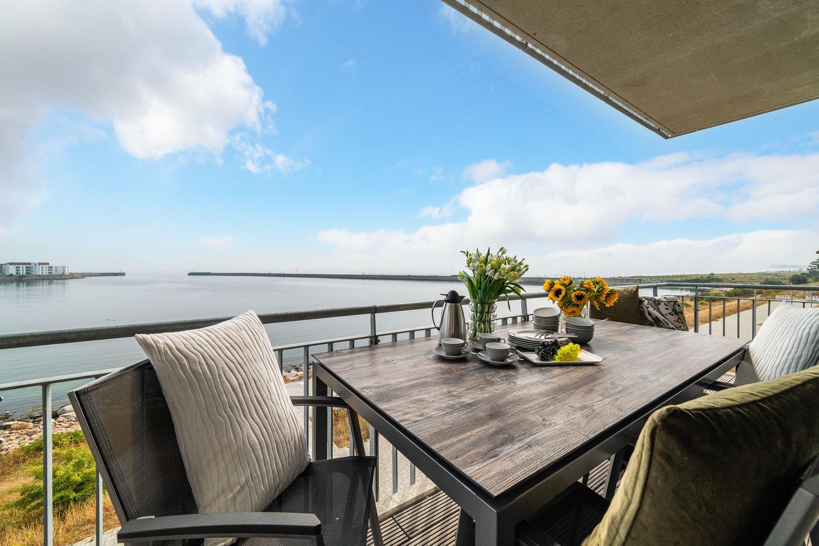 Terrasse mit Tisch, Stühlen und Meerblick. Blumen und Früchte auf dem Tisch.