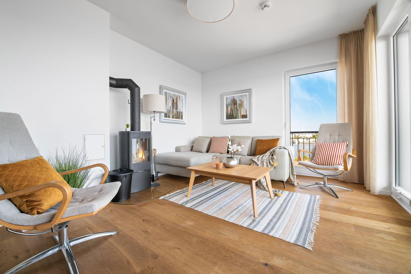 Wohnzimmer mit Kamin, Sofa, zwei Sessel und Holzboden. Blick auf Balkon mit Stadtblick.