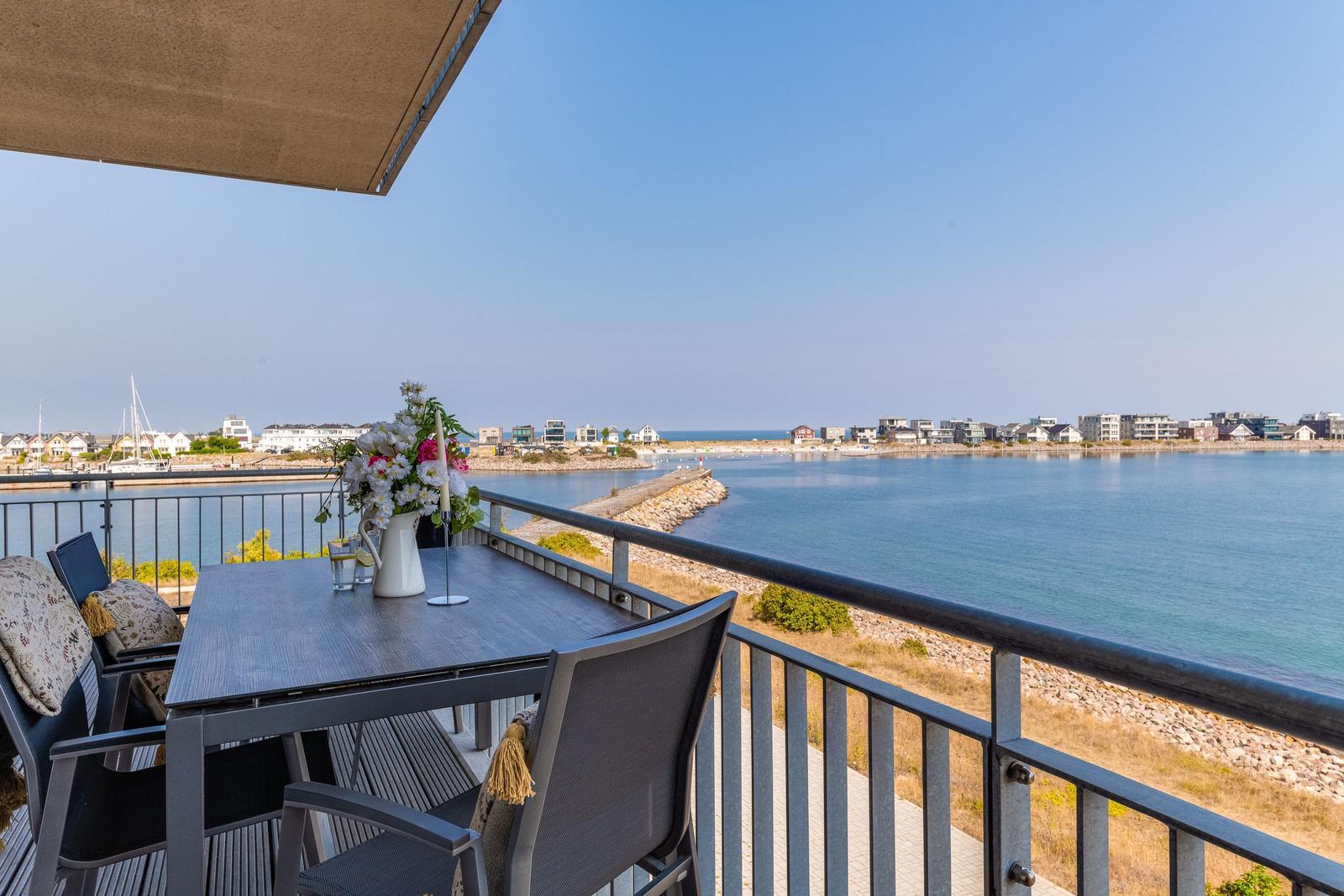Terrasse mit Tisch und Stühlen, Blick auf Hafen und Küste.