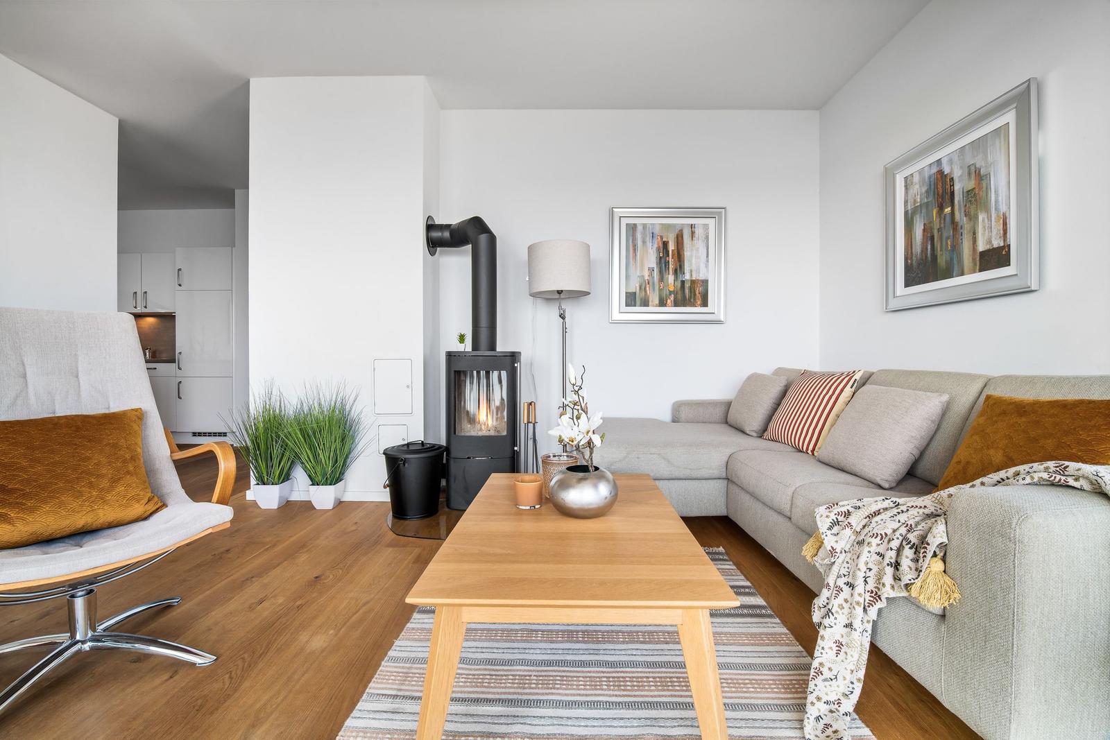 Wohnzimmer mit Sofa, Kaminofen und Holztisch. Küche im Hintergrund.