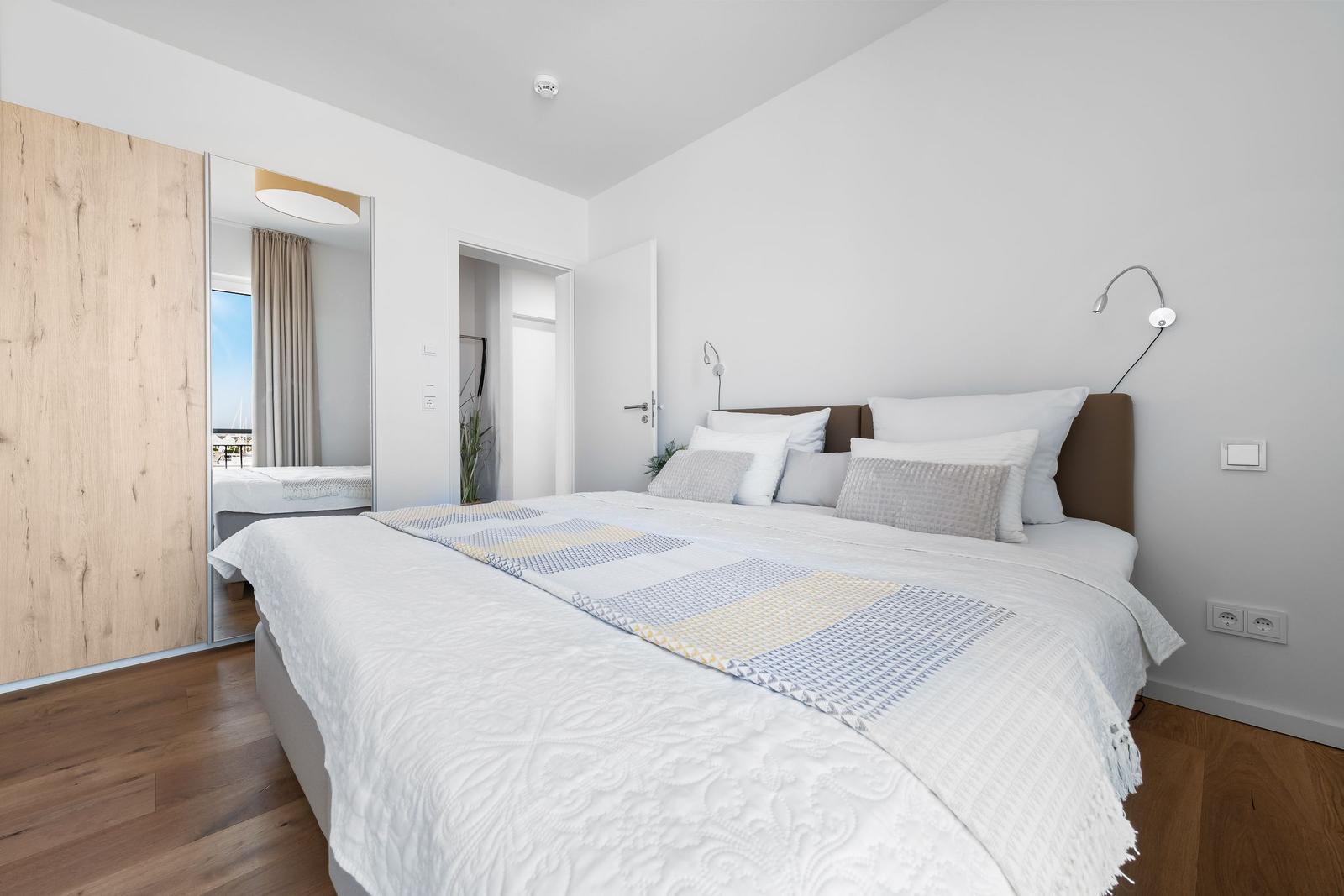 Schlafzimmer mit Doppelbett, Spiegelschrank und Blick auf Balkon.