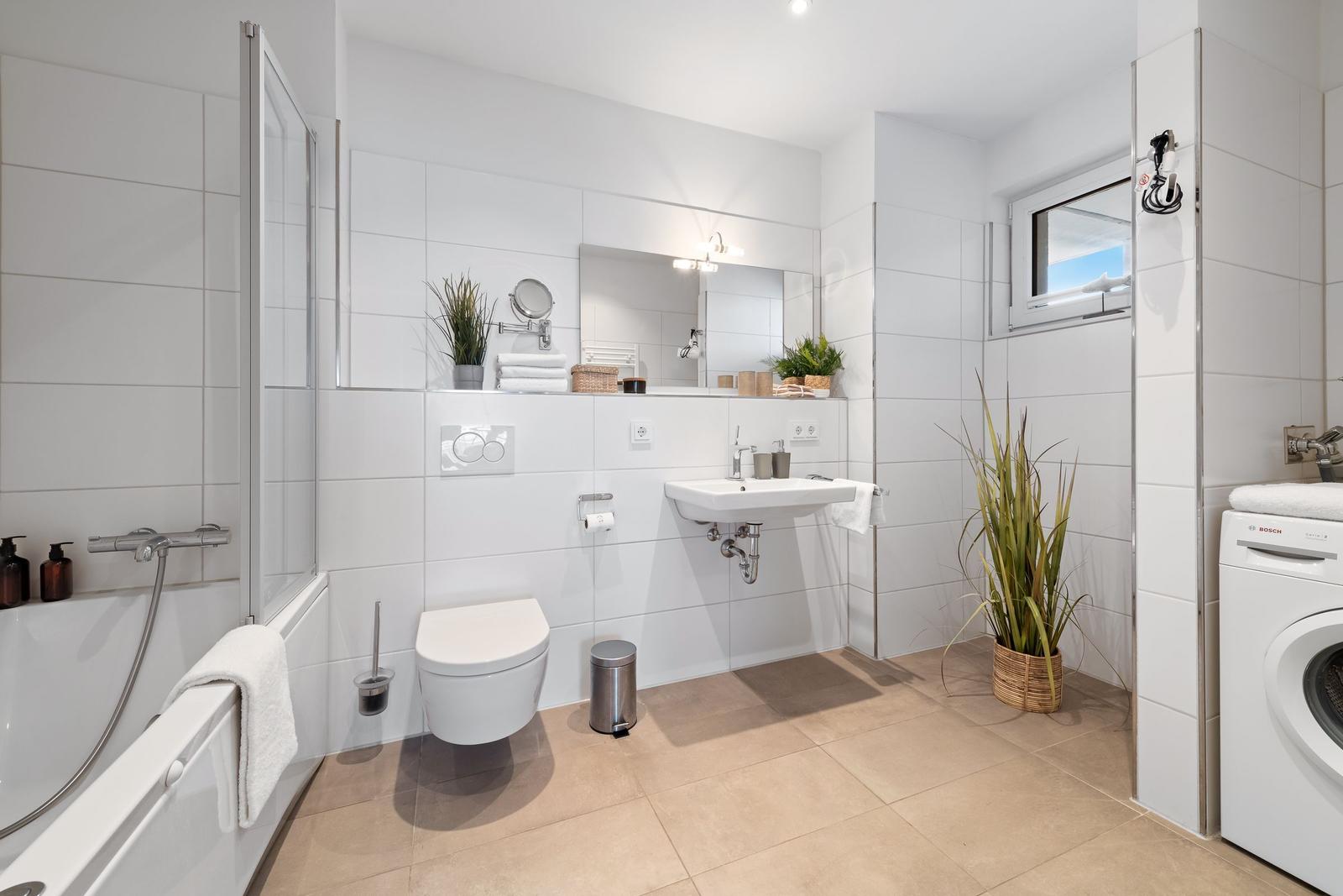Badezimmer mit Badewanne, Dusche, Waschmaschine und Pflanzen.