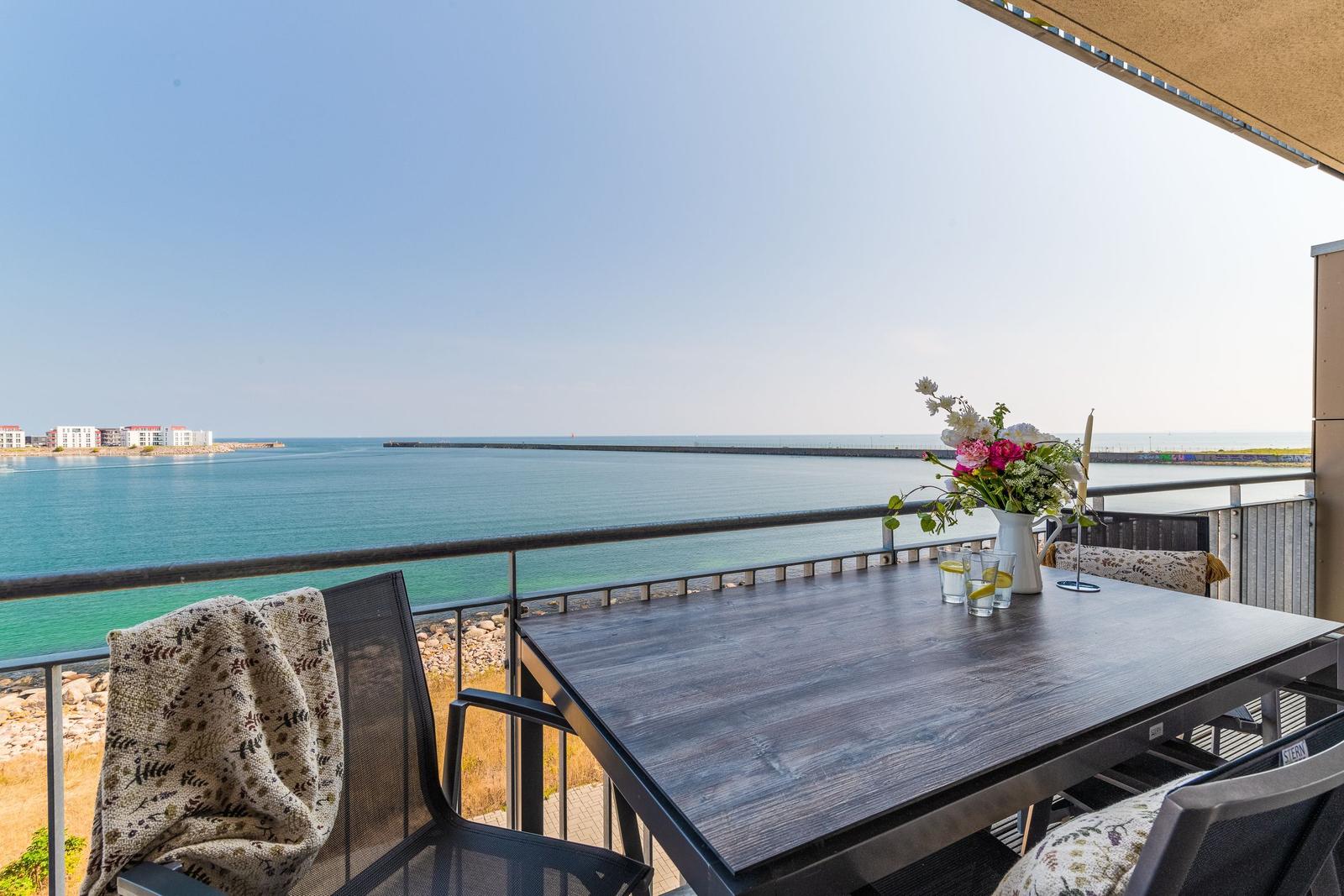 Terrasse mit Tisch, Stühlen und Meerblick. Blumen und Getränke auf dem Tisch.