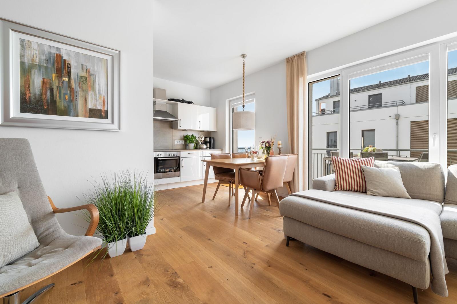 Wohnbereich mit Essbereich und Küche. Holzboden, Sofa, Essgruppe und Fenster zum Balkon.