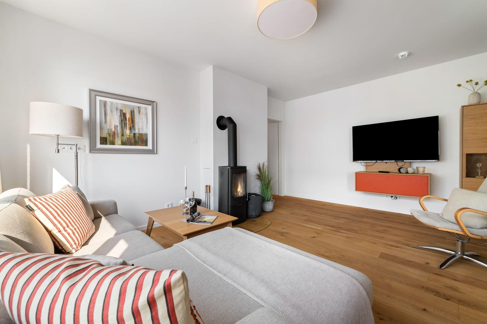 Wohnzimmer mit Sofa, Kaminofen, Fernseher und Holzboden.