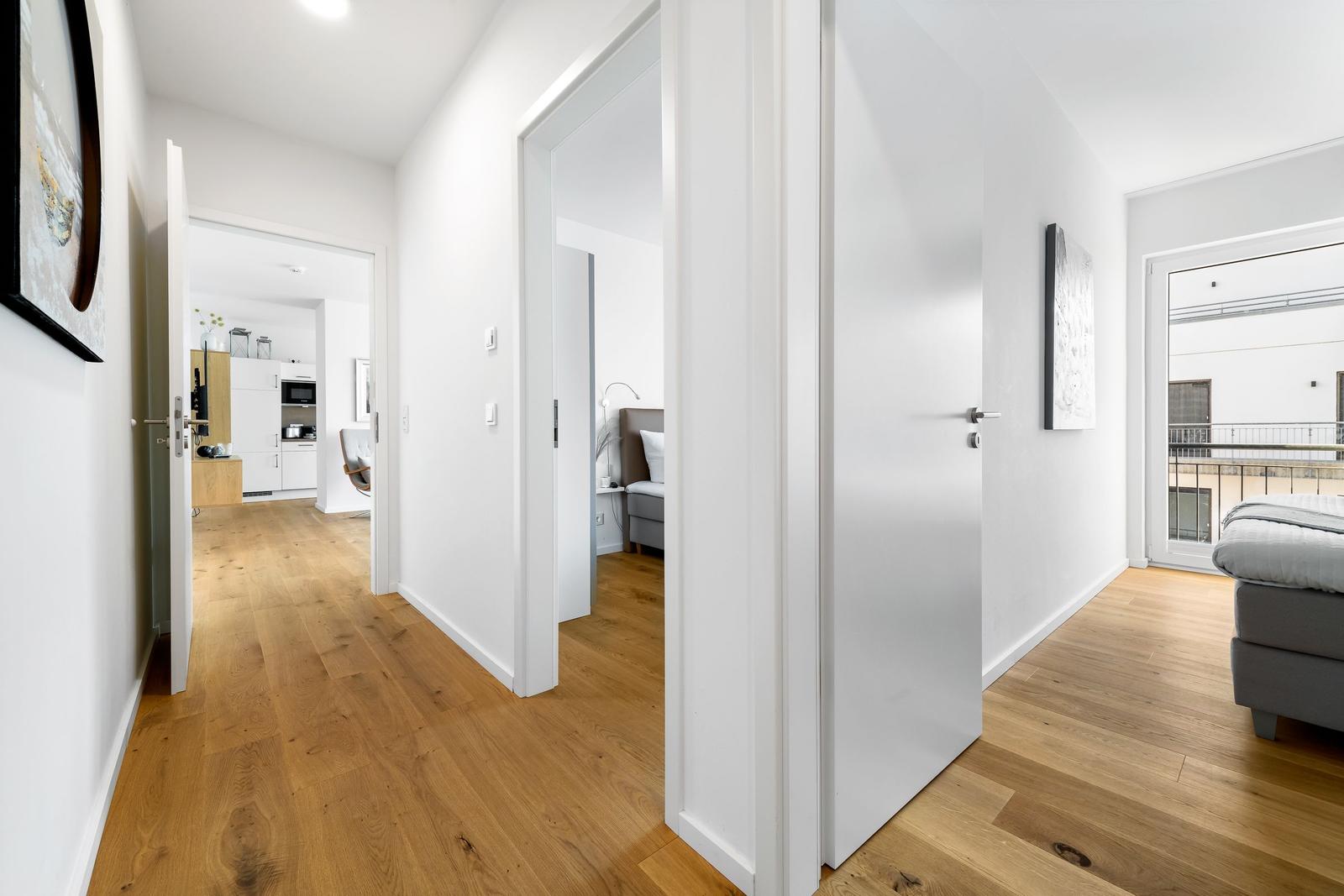 Flur mit Holzboden, Blick in Küche, Schlafzimmer und Wohnbereich mit Balkon.