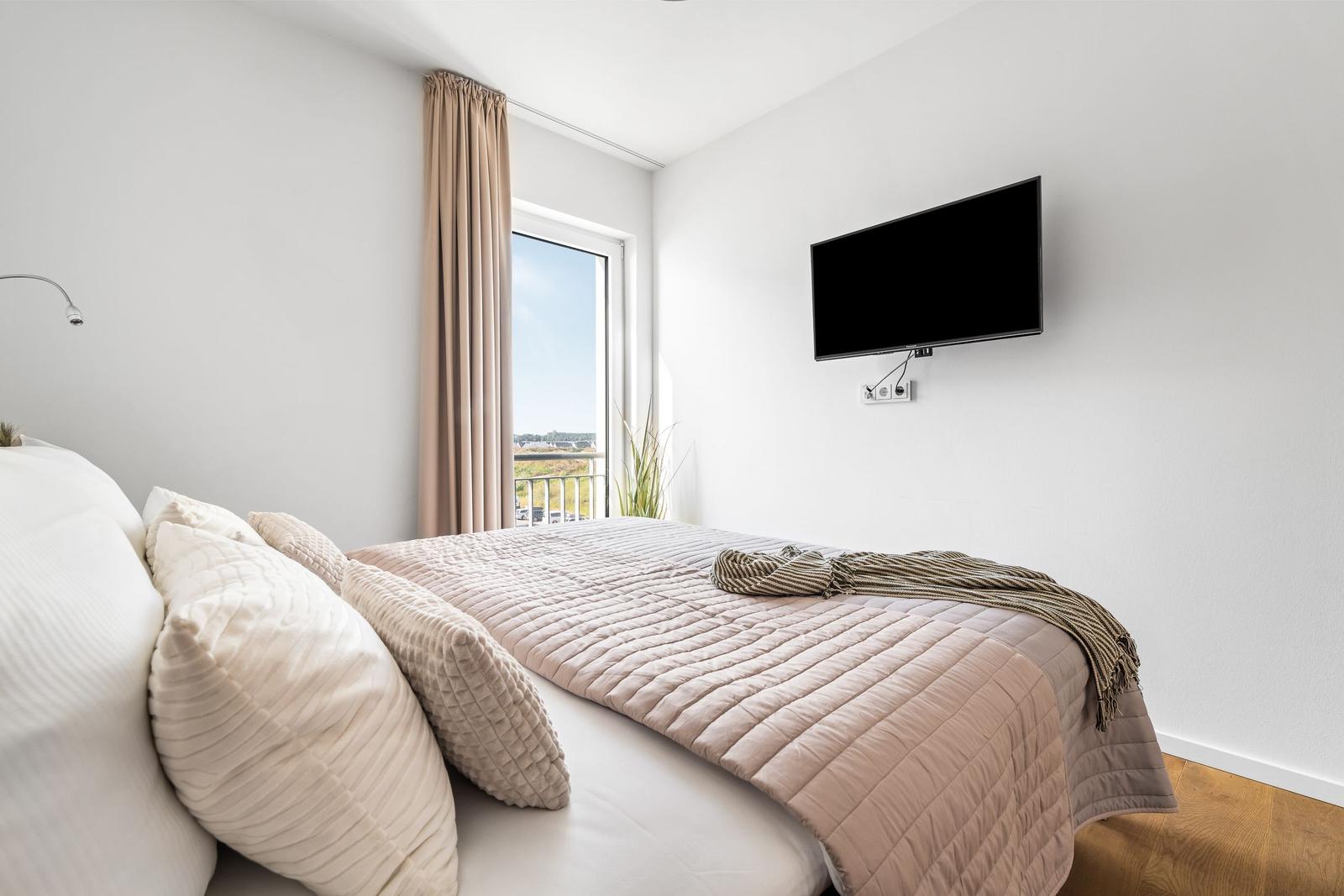 Schlafzimmer mit Bett, TV und Balkonansicht.