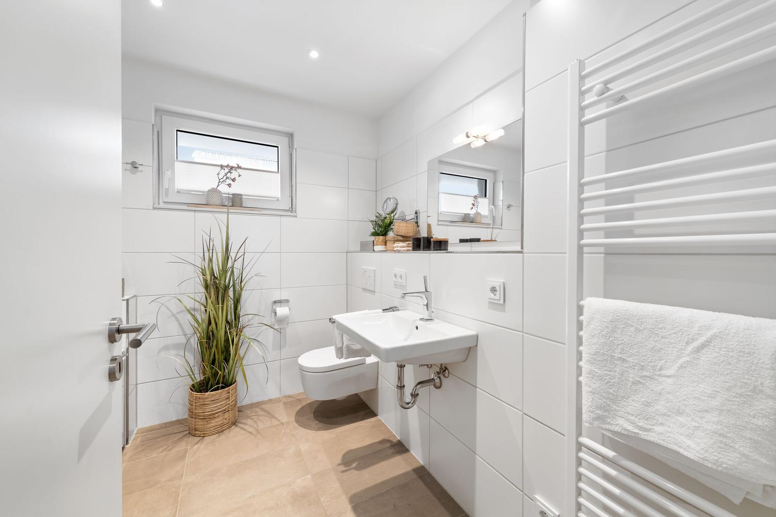 Badezimmer mit Toilette, Waschbecken und Heizung. Fenster mit Pflanze und Spiegel.