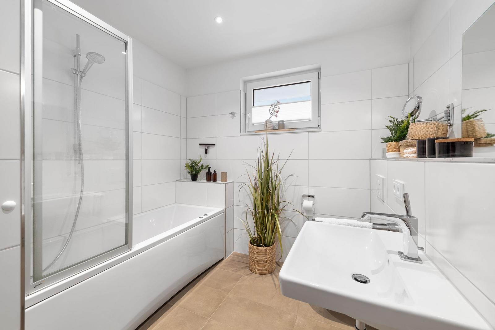 Badezimmer mit Badewanne, Dusche, Waschbecken und Pflanzen.