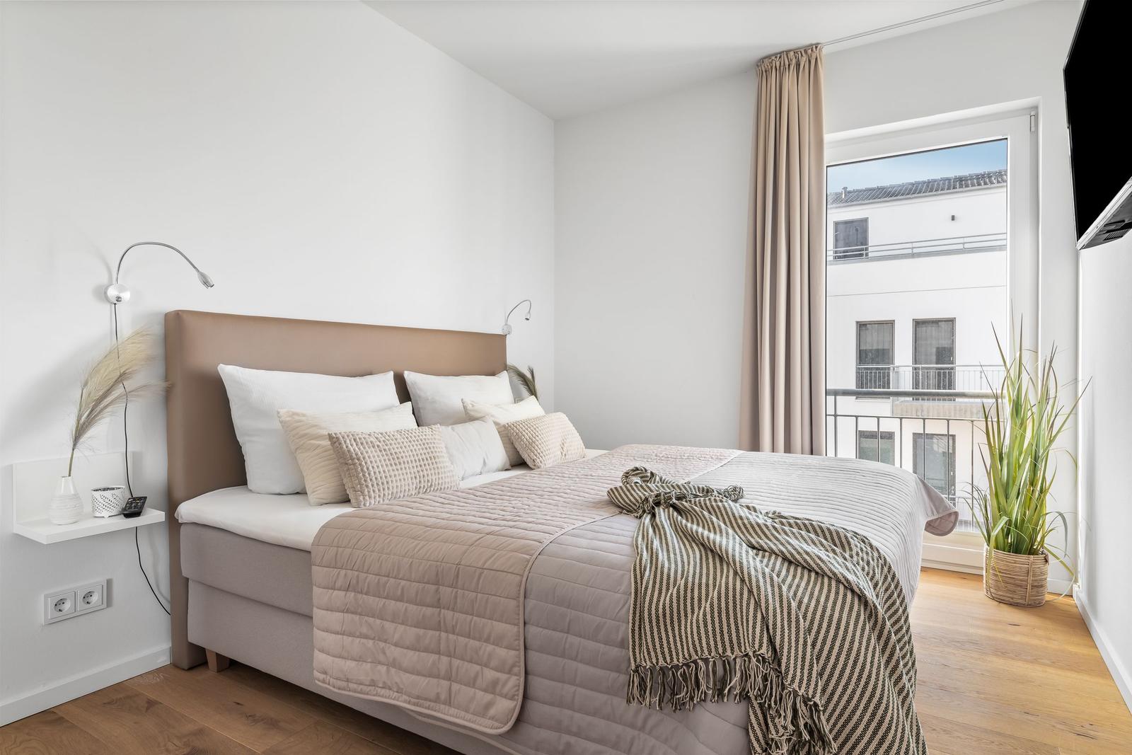 Schlafzimmer mit Bett, Fenster und Pflanze.