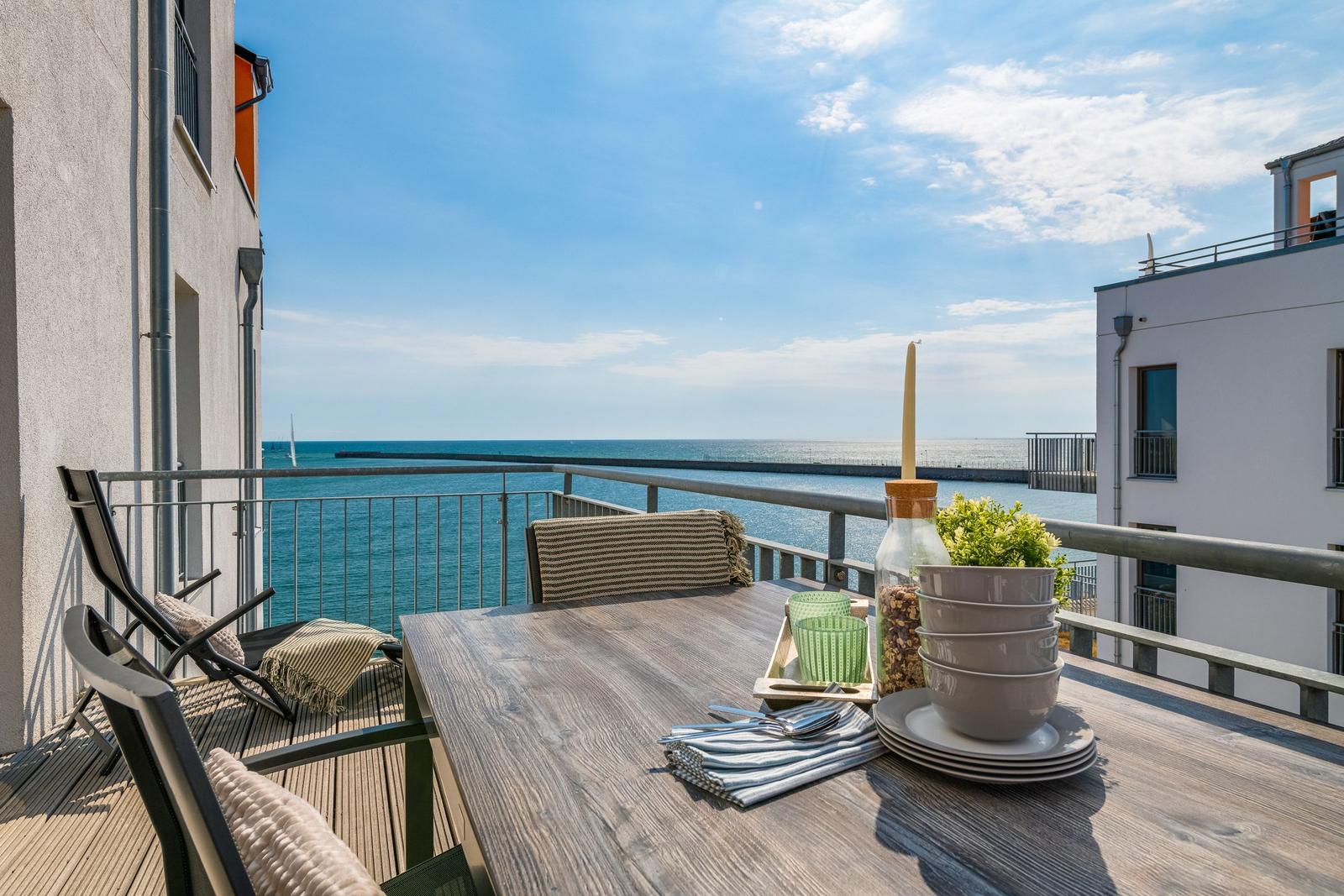 Terrasse mit Tisch, Stühlen und Meerblick. Tisch mit Geschirr und Pflanze.