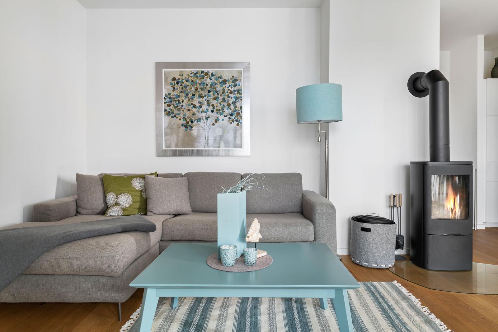 Ein Wohnzimmer mit grauem Sofa, blauem Couchtisch und Kaminofen.