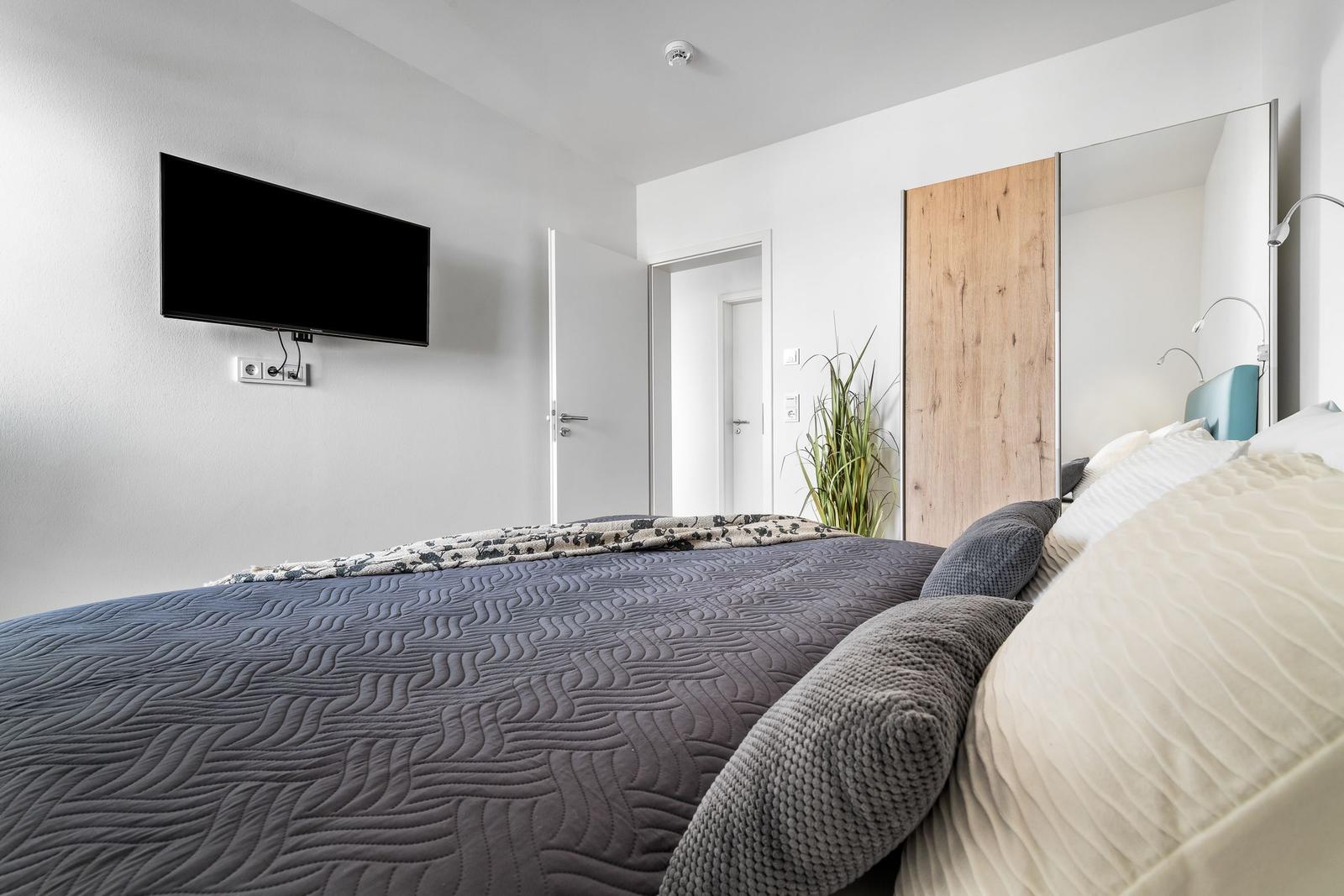 Schlafzimmer mit Bett, Fernseher an der Wand und Spiegel.