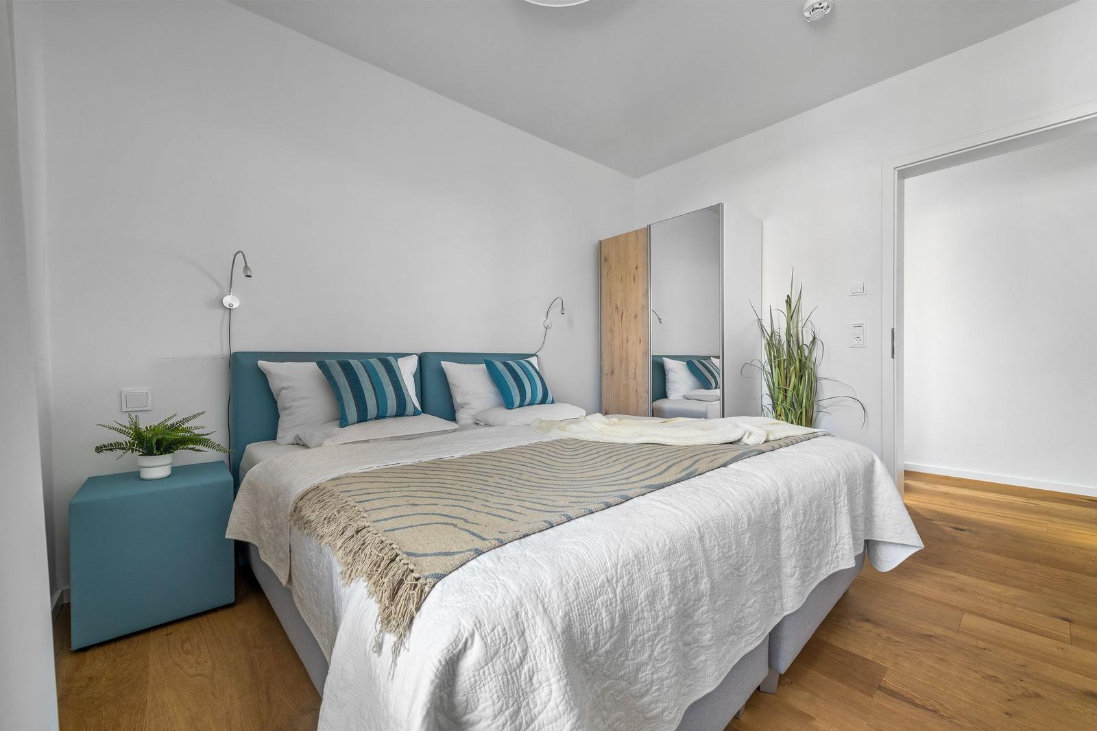 Schlafzimmer mit Bett, Nachttisch, Spiegel und Pflanzen.