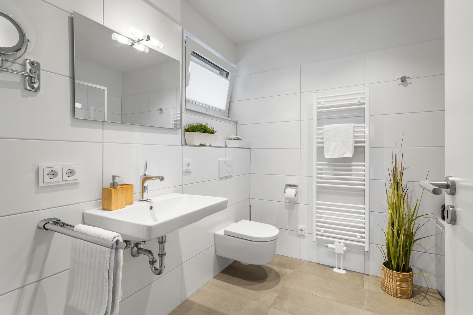 Badezimmer mit Waschbecken, Spiegel, Toilette und Heizung. Pflanze und Handtuchhalter sichtbar.