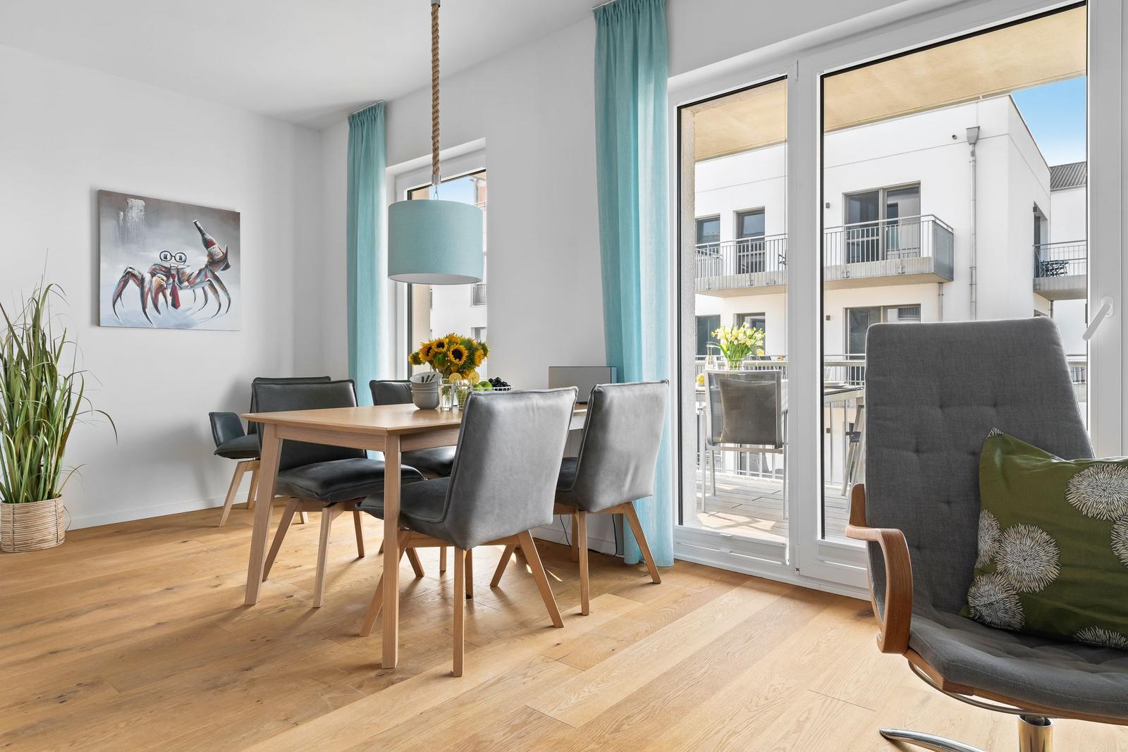 Essbereich mit Tisch, Stühlen und Blick auf Balkon. Wandbild und Pflanze sichtbar.