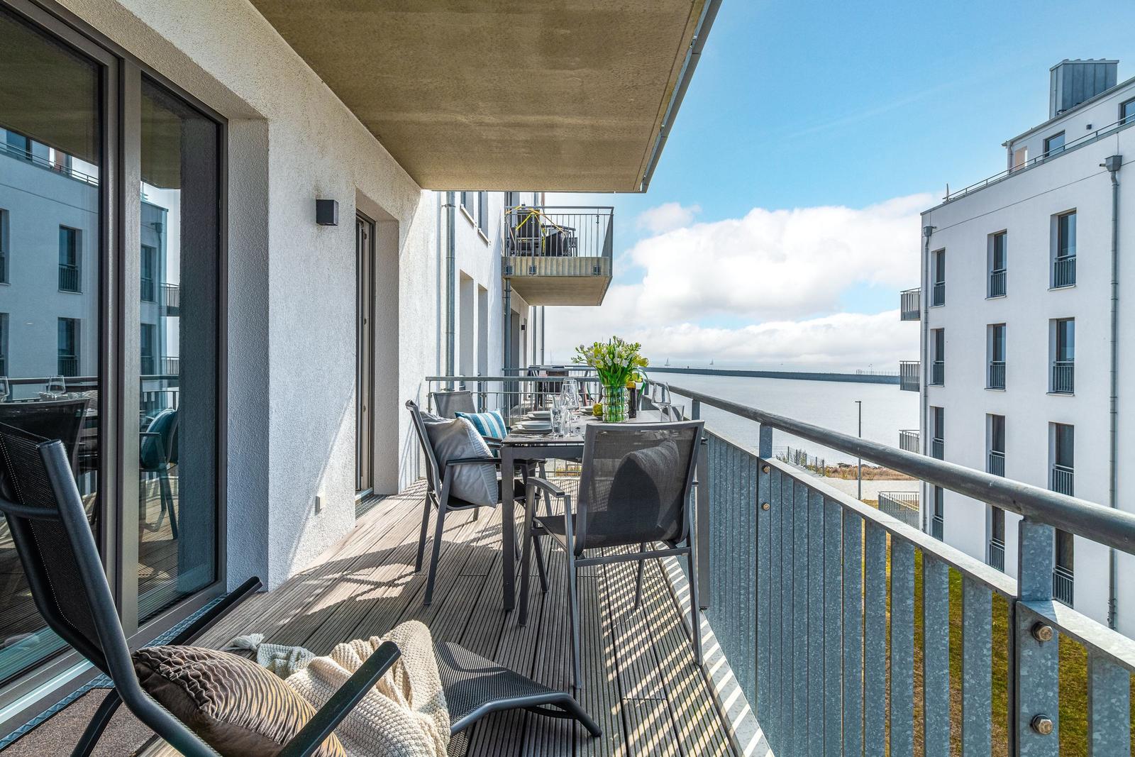 Terrasse mit Tisch, Stühlen und Meerblick. Holzdielen und Metallgeländer.