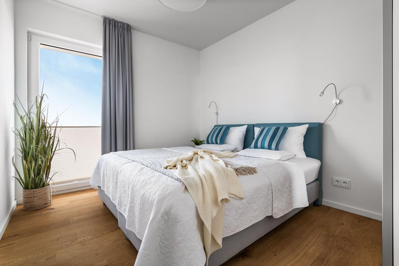 Schlafzimmer mit Doppelbett, Fenster und Pflanze.
