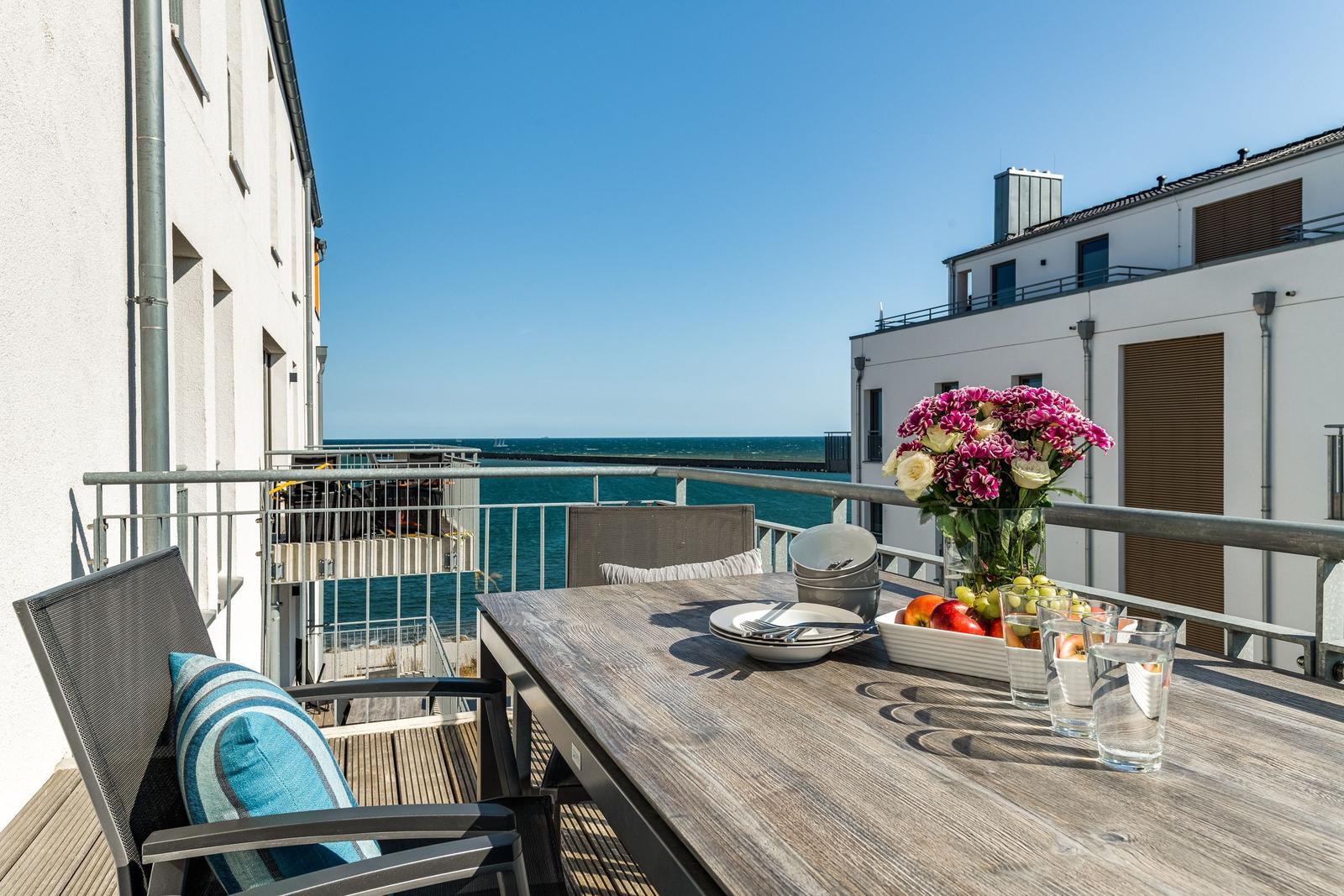 Terrace with table, chairs, and sea view. Flowers and fruit on the table.
