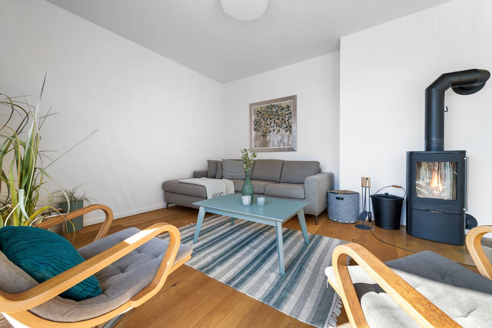 Living room with sofa, fireplace, and wooden floor. Two chairs and rug are visible.