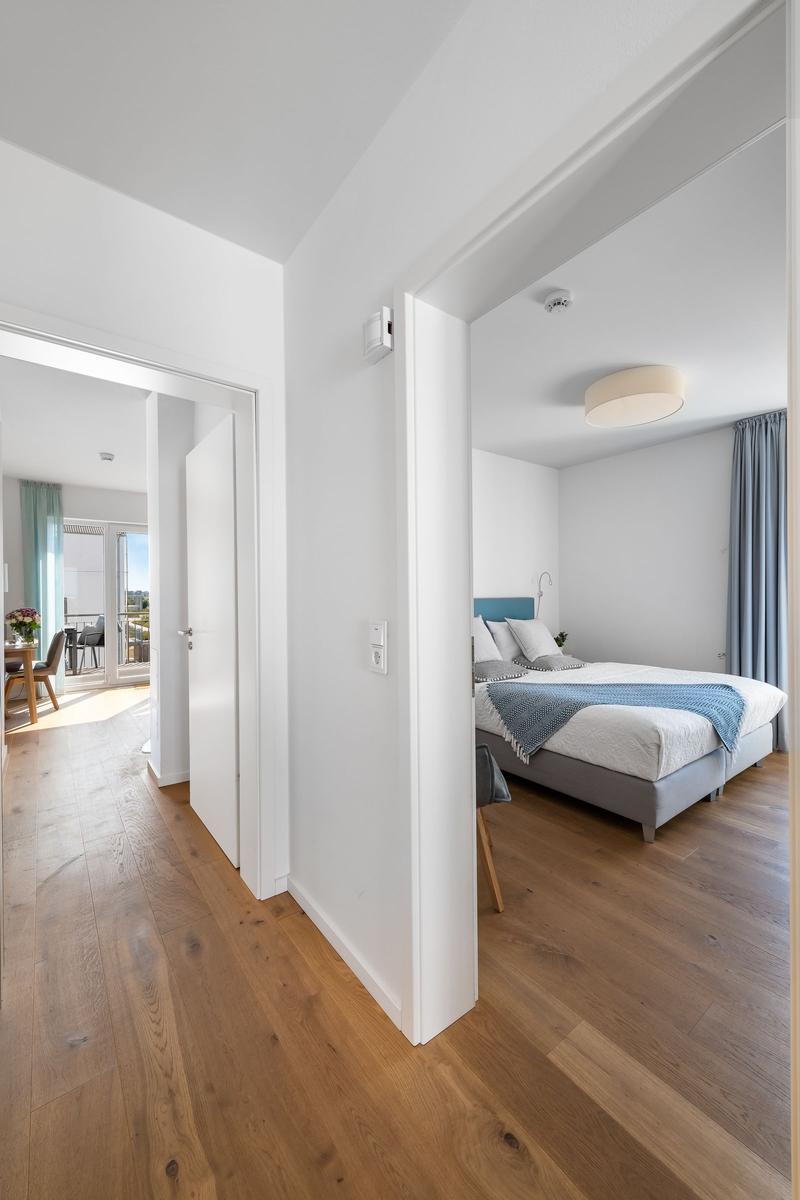 Bedroom with bed and view into living area with dining space and balcony.