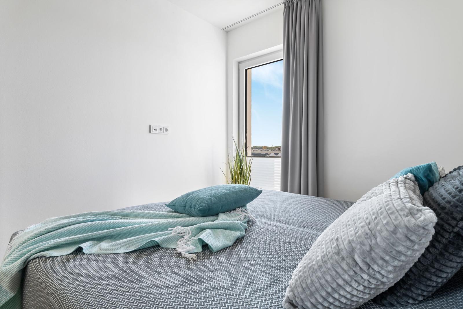Bedroom with bed, pillows, and view of outside through window.